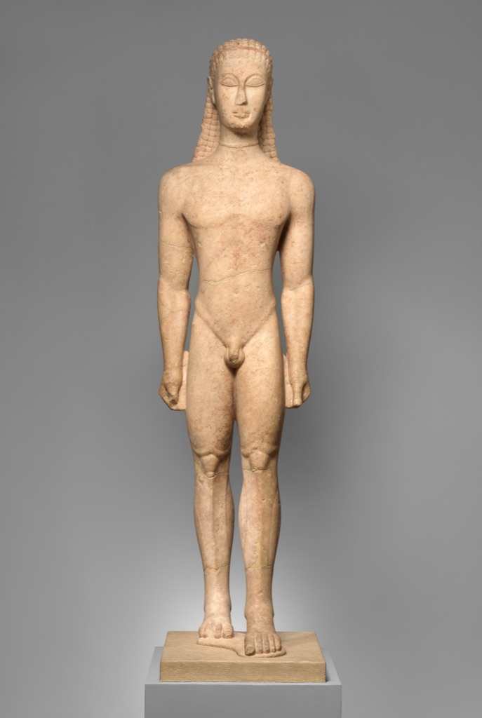An ancient Greek marble kouros stands frontally with arms at his sides and one foot advanced.