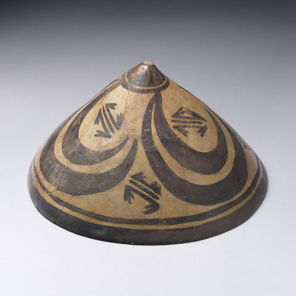 A conical ancient Iranian painted bowl, shown obliquely, carries four dark ibex-horn forms around its pointed centre.