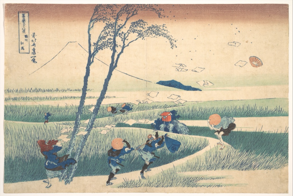 Hokusai's Ejiri shows travellers bracing against wind as papers and leaves fly past bent trees below Mount Fuji.