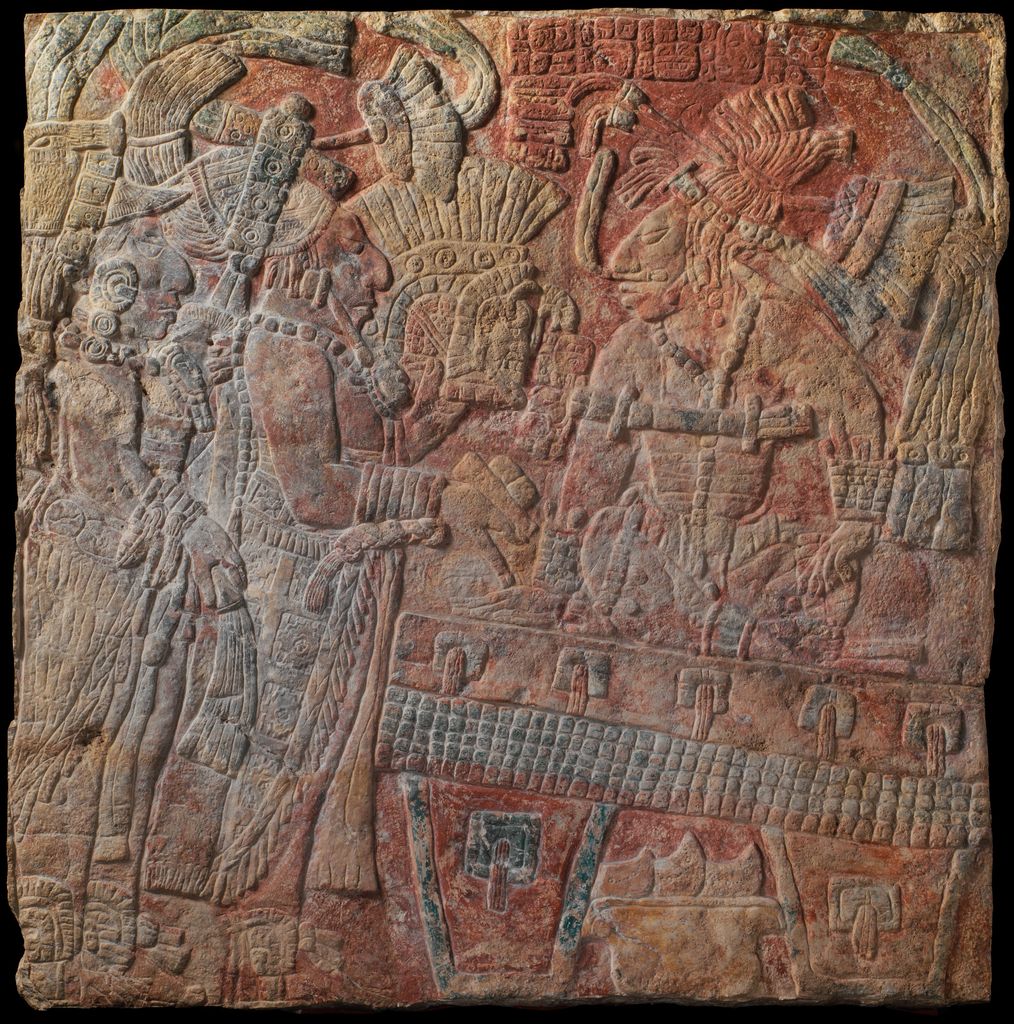 A square limestone relief shows an enthroned Maya ruler surrounded by carved bands, smaller forms and traces of paint.