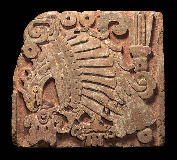 Toltec stone relief of an eagle biting a stylised human heart, with layered feathers and traces of colour.
