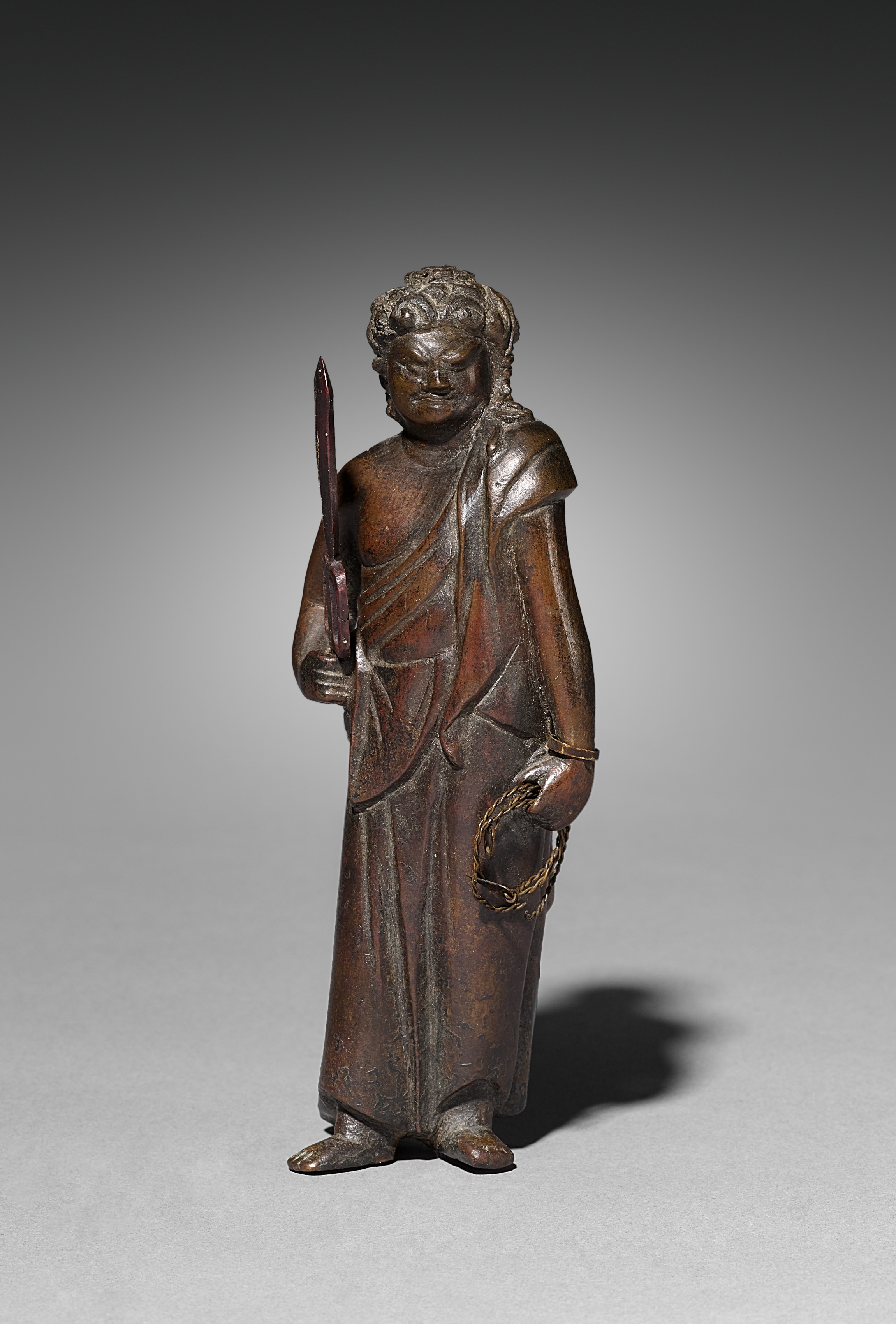 Small standing Japanese bronze Fudō Myōō holding a sword and a looped chain, with wire attachments visible at the wrist and hand.