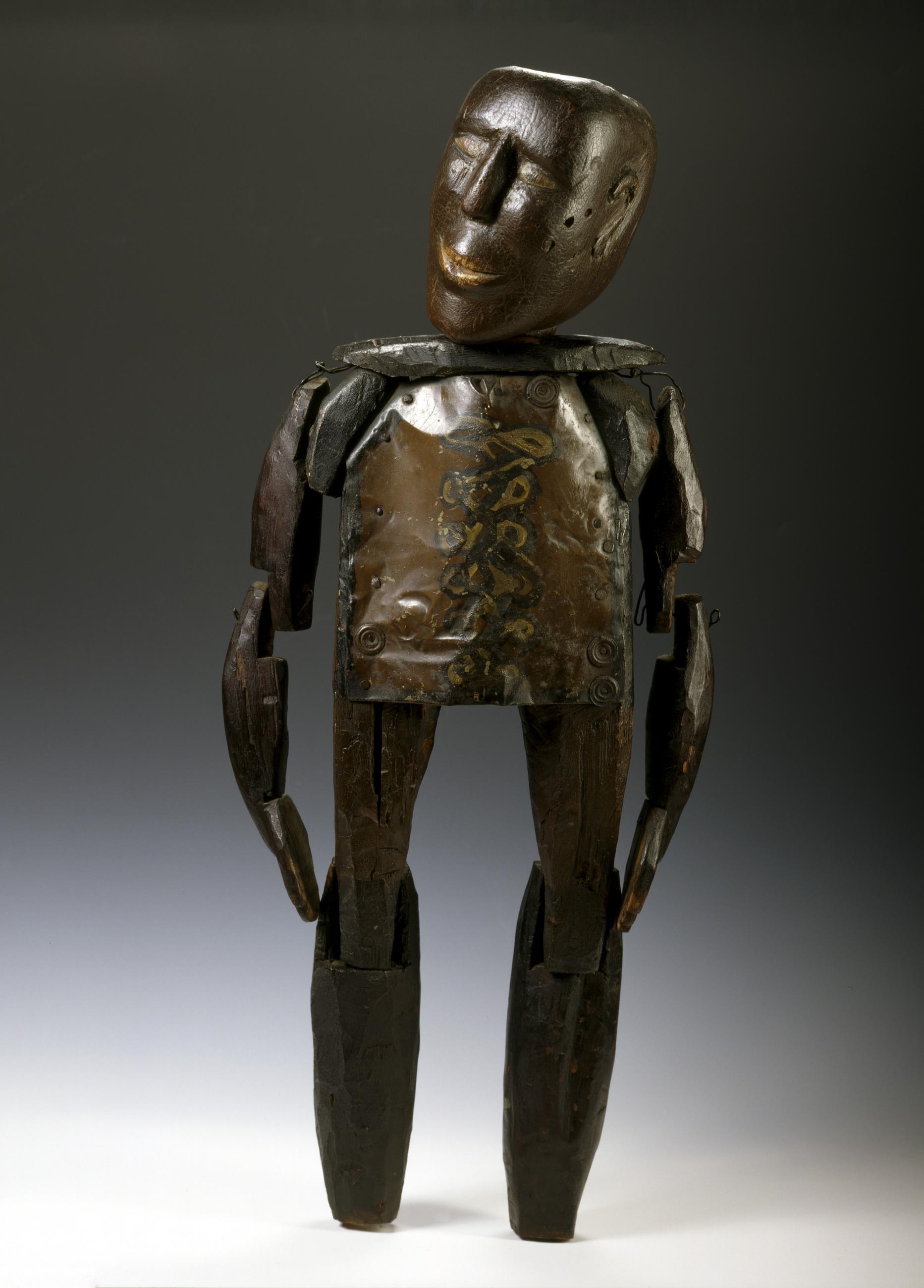 Standing articulated wooden figure with a carved head, long jointed limbs and a painted metal torso connected by visible wire and hardware.