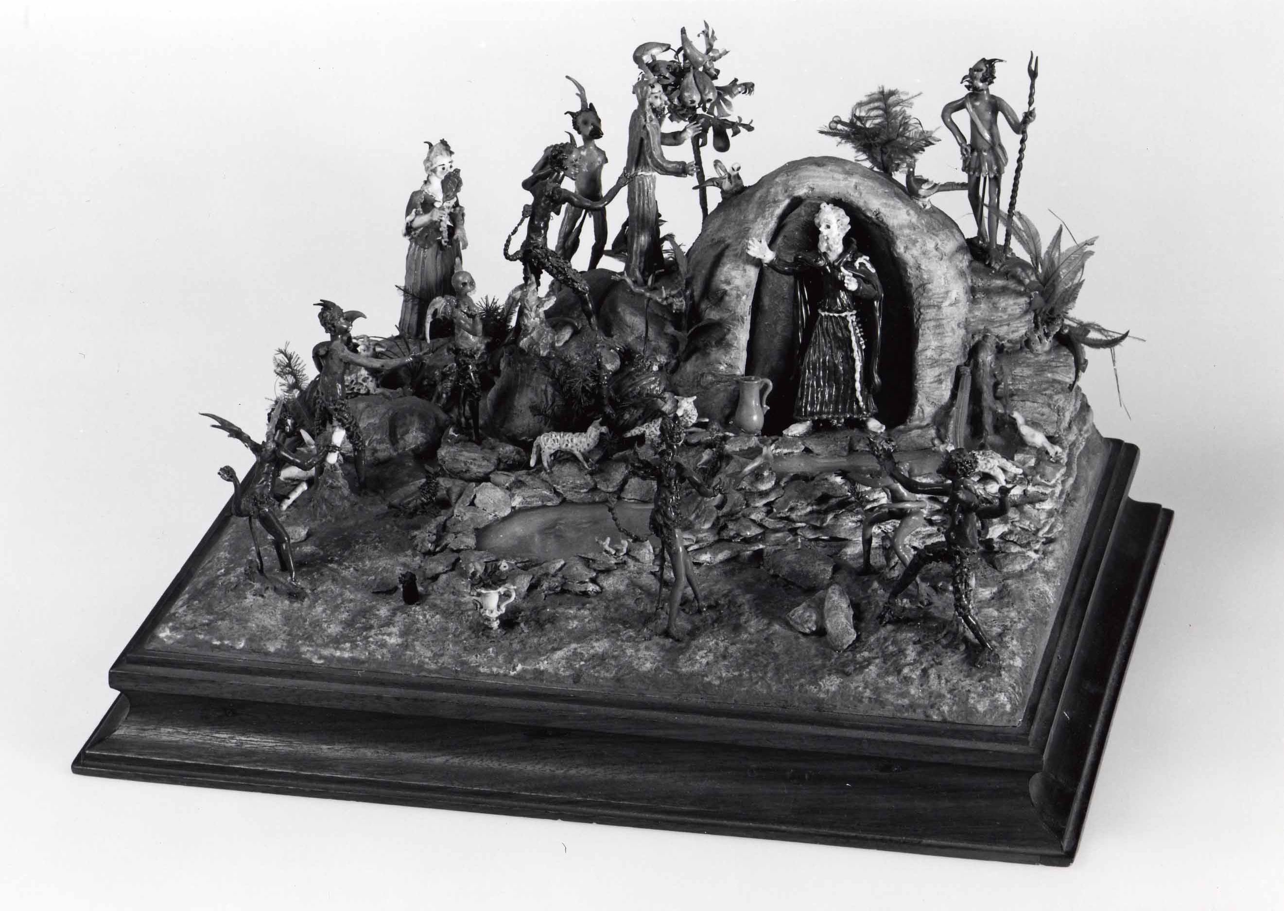 Wide assembled tableau of Saint Anthony surrounded by many small lampworked-glass figures and animals on a rocky landscape.